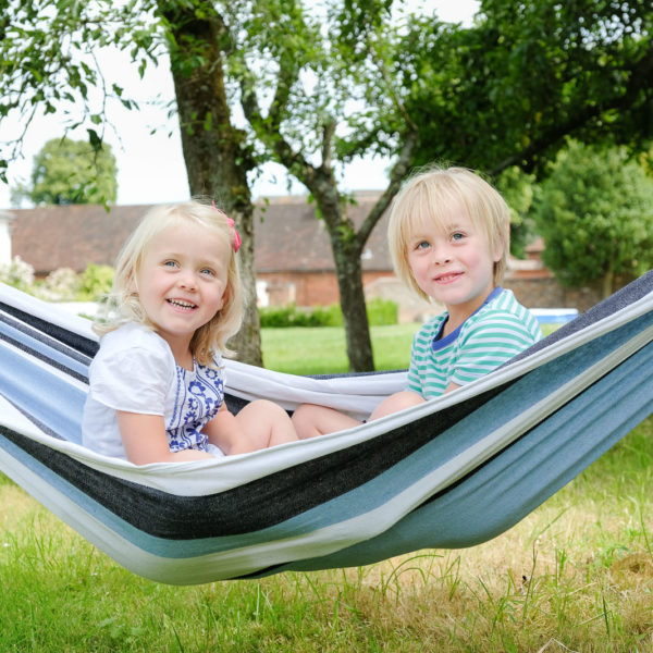 Family photography with young brother and sister playing in hammock in back garden