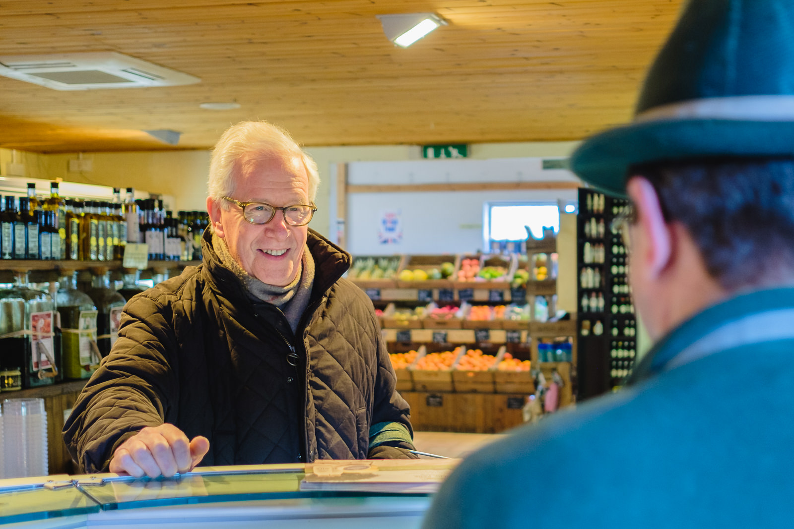 Corporate marketing photography with customer talking to staff on the deli counter at Allington Farm Shop in Wiltshire