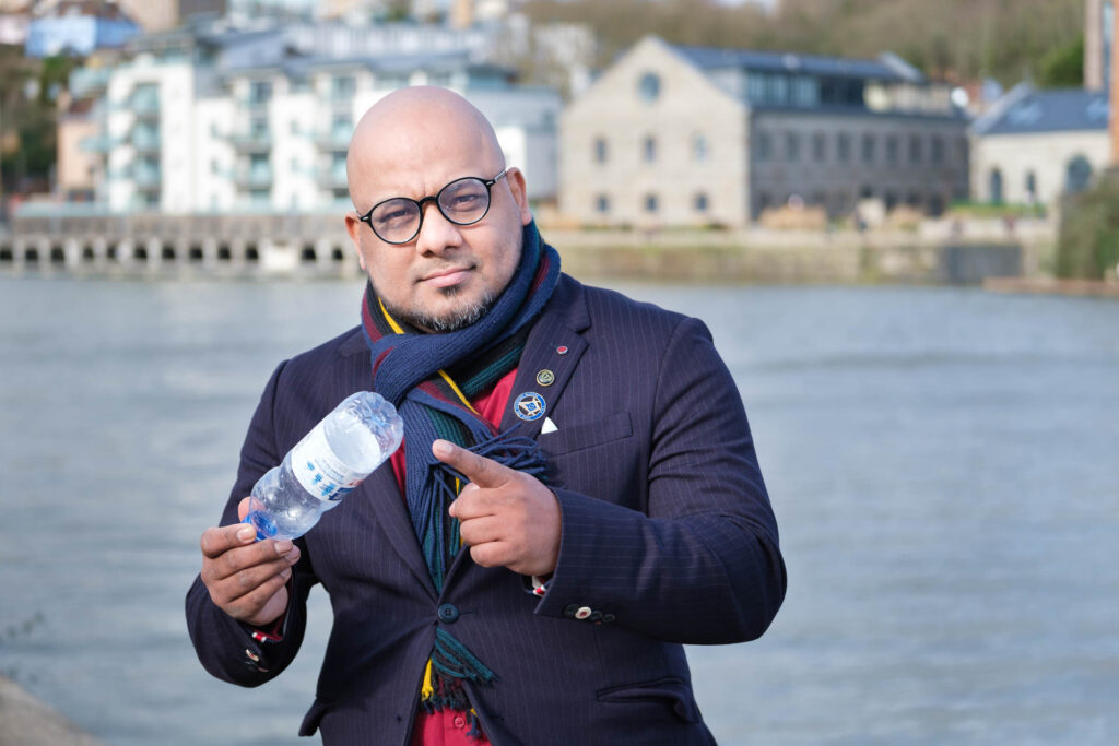 Branding photo of Naseem Talukdar holding a waste plastic bottle on the Bristol harbourside