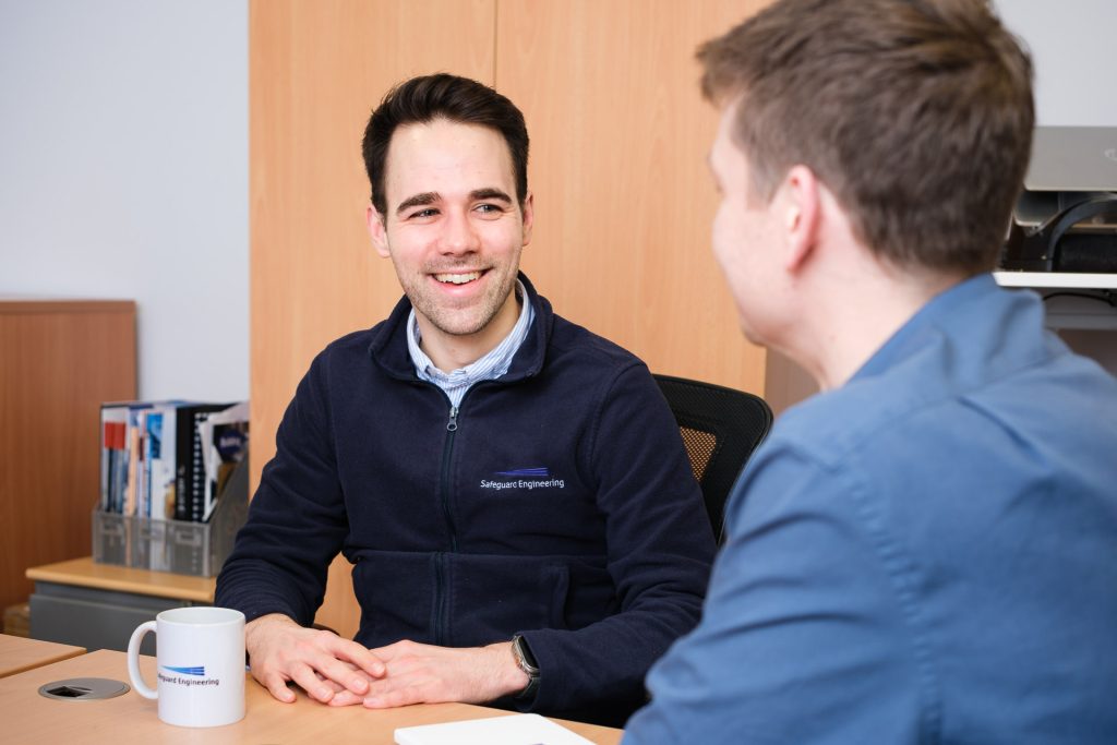 Two young male engineering consultants at the desk in conversation with each other