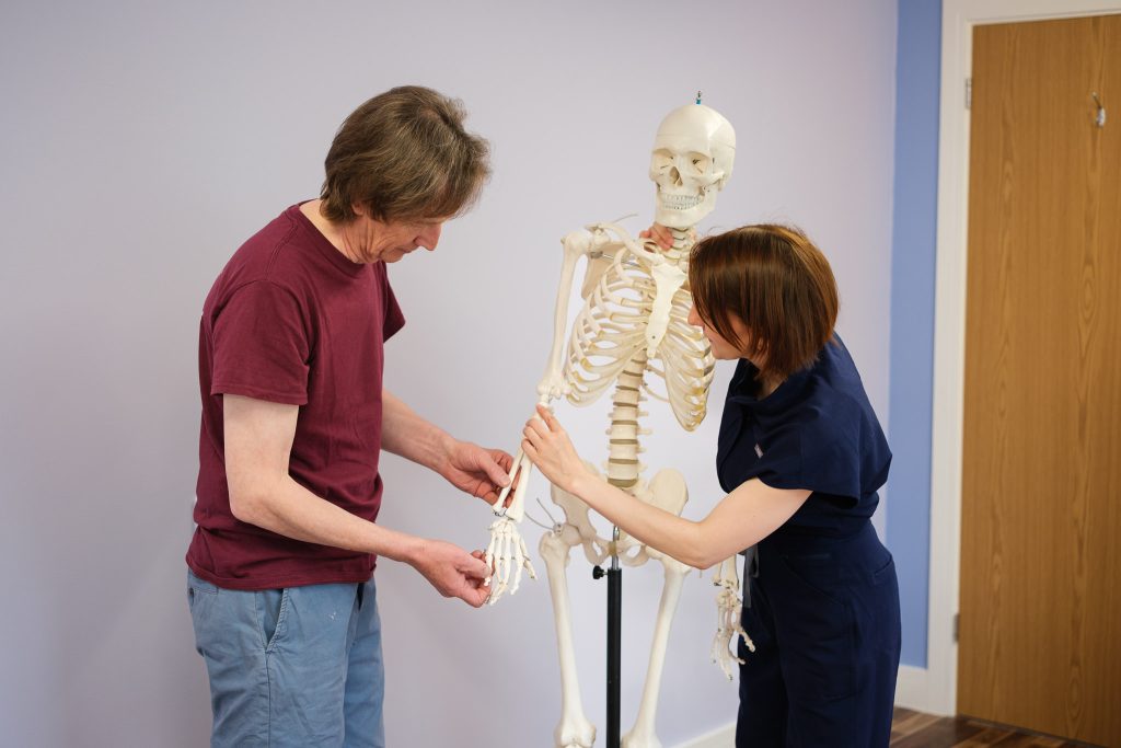 Female osteopath explaining an arm injury to a male client using a plastic skeleton