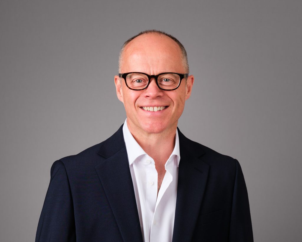 Relaxed business headshot - UK sales director with open neck white shirt and a dark navy jacket.