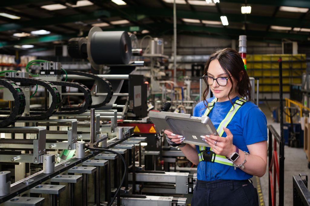 Manufacturing photography showing a female operative reviewing line performance on a hand held tablet