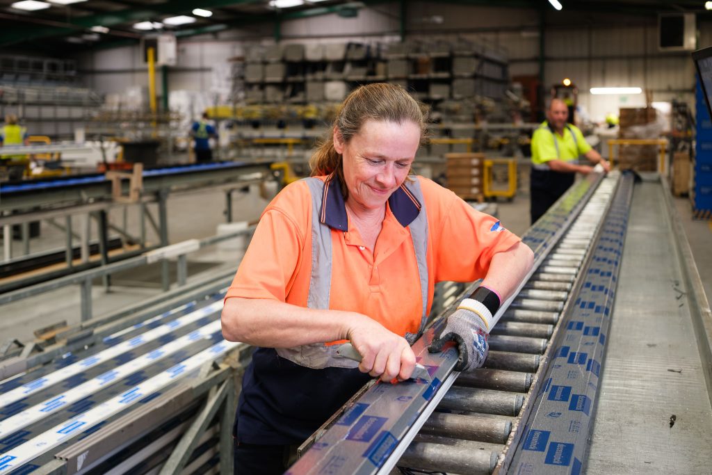 Manufacturing photography showing a female production operative cutting a window frame on a fast moving production line